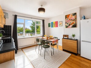 A modern kitchen with a dining area, large windows, and a view of greenery outside. - Spacious 3BR Flat Sleeps 7 in Greenford (London)