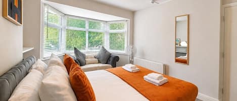 A hotel room with a bed, a window with blinds, a radiator, a mirror, and a fan.