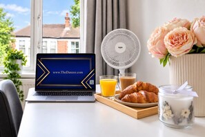 A laptop with a website displayed, a fan, a tray with croissants, a glass of orange juice, a glass of coffee, and a candle. - Spacious 3BR Flat Sleeps 7 in Greenford (London)