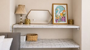 Een kamer met een witte bakstenen muur, een grijze bank, een witte lamp, een goudkleurige geometrische vaas, een ingelijste foto van een zwaan, en een geweven mandje op een witte plank.