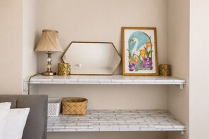 A room with a white brick wall, a grey sofa, a white lamp, a gold-colored geometric vase, a framed picture of a swan, and a woven basket on a white shelf. - Spacious 3BR Flat Sleeps 7 in Greenford (London)