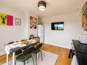 A compact kitchen with a dining area, a refrigerator, a microwave, and a television. - Spacious 3BR Flat Sleeps 7 in Greenford (London)