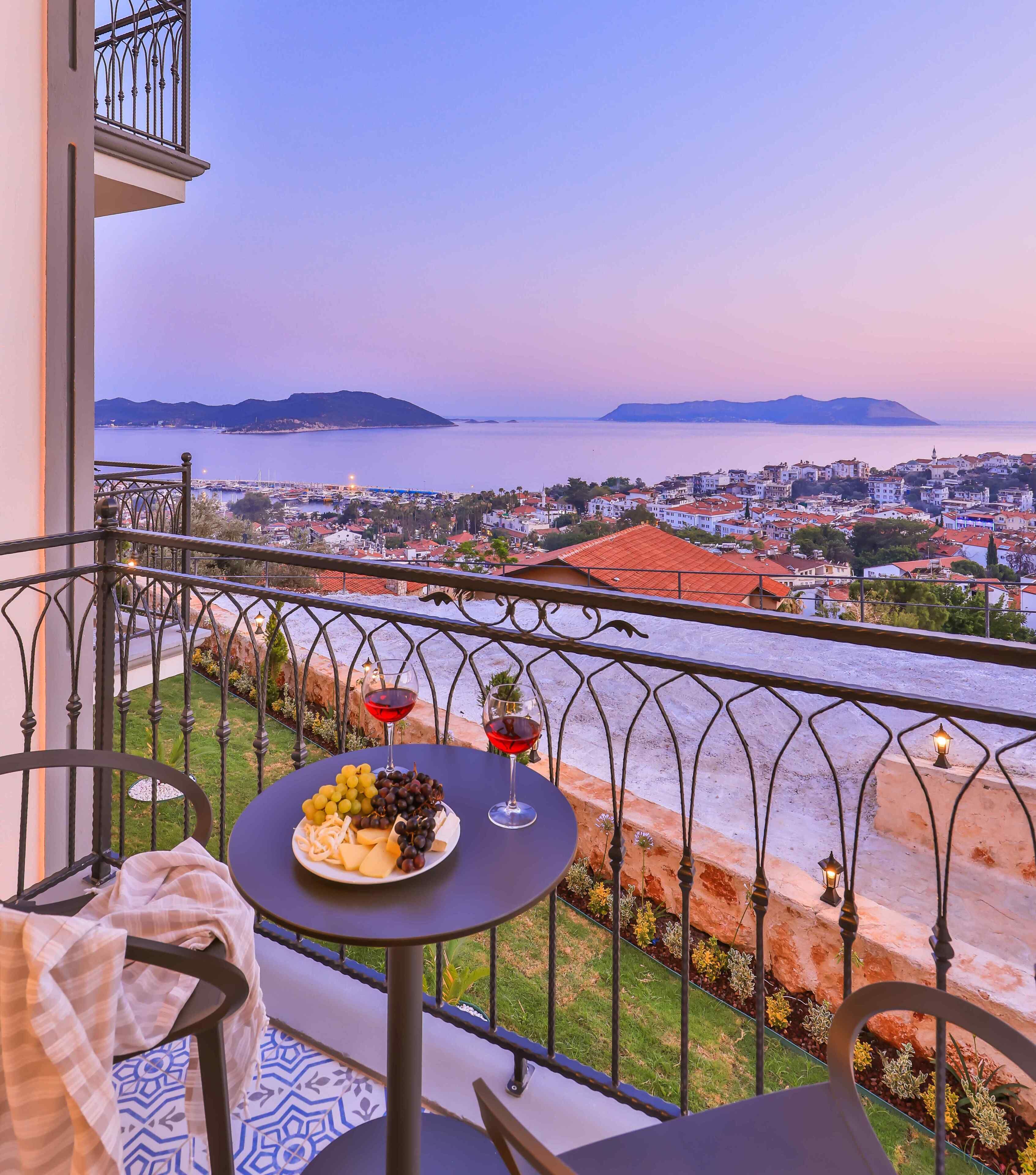 Un balcone con un tavolo apparecchiato per due, vista su una cittadina costiera e ringhiera con decorazioni.