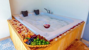 A bathtub with rose petals, a glass of red wine, and a basket of fruit.
