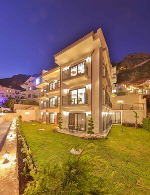 A multi-story hotel with balconies, a well-lit lawn, and a mountain backdrop. - Lobelya Suites  (Kas)