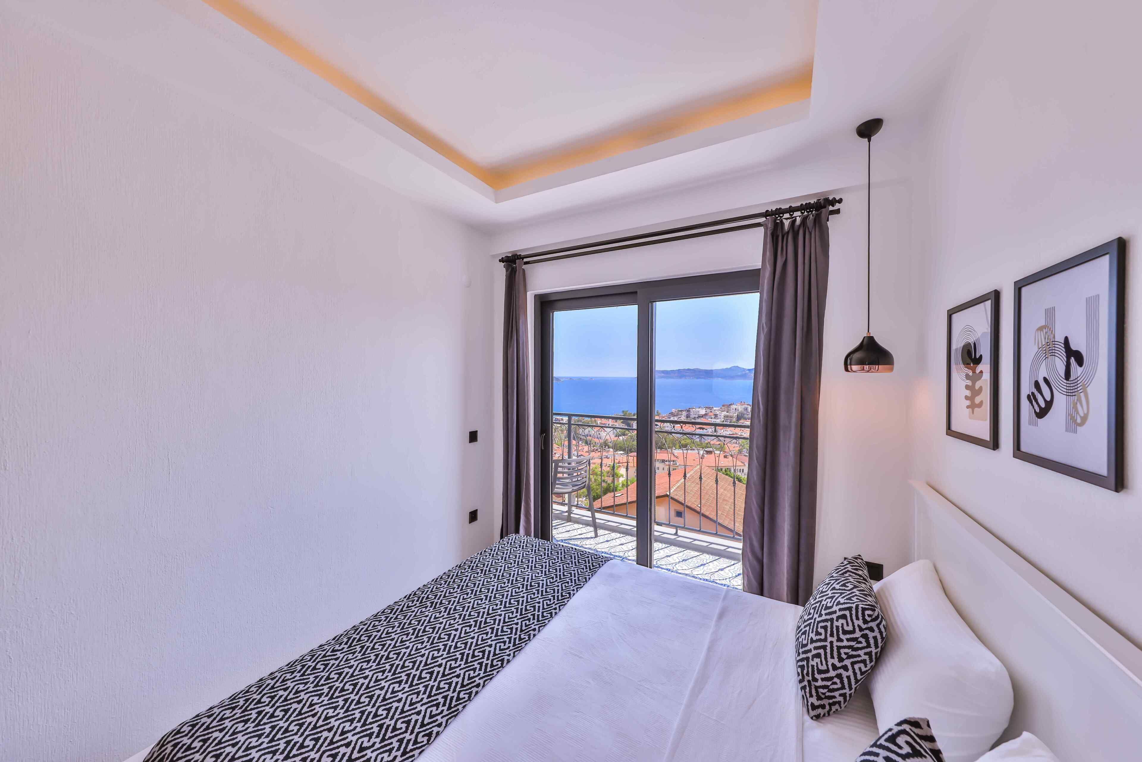 A hotel room with a bed, a view of the sea, and a balcony with a chair.