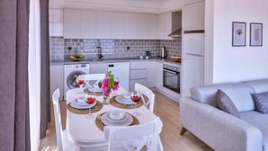 Une cuisine moderne avec des armoires blanches, un four encastré et un coin repas avec une table dressée pour quatre personnes.
