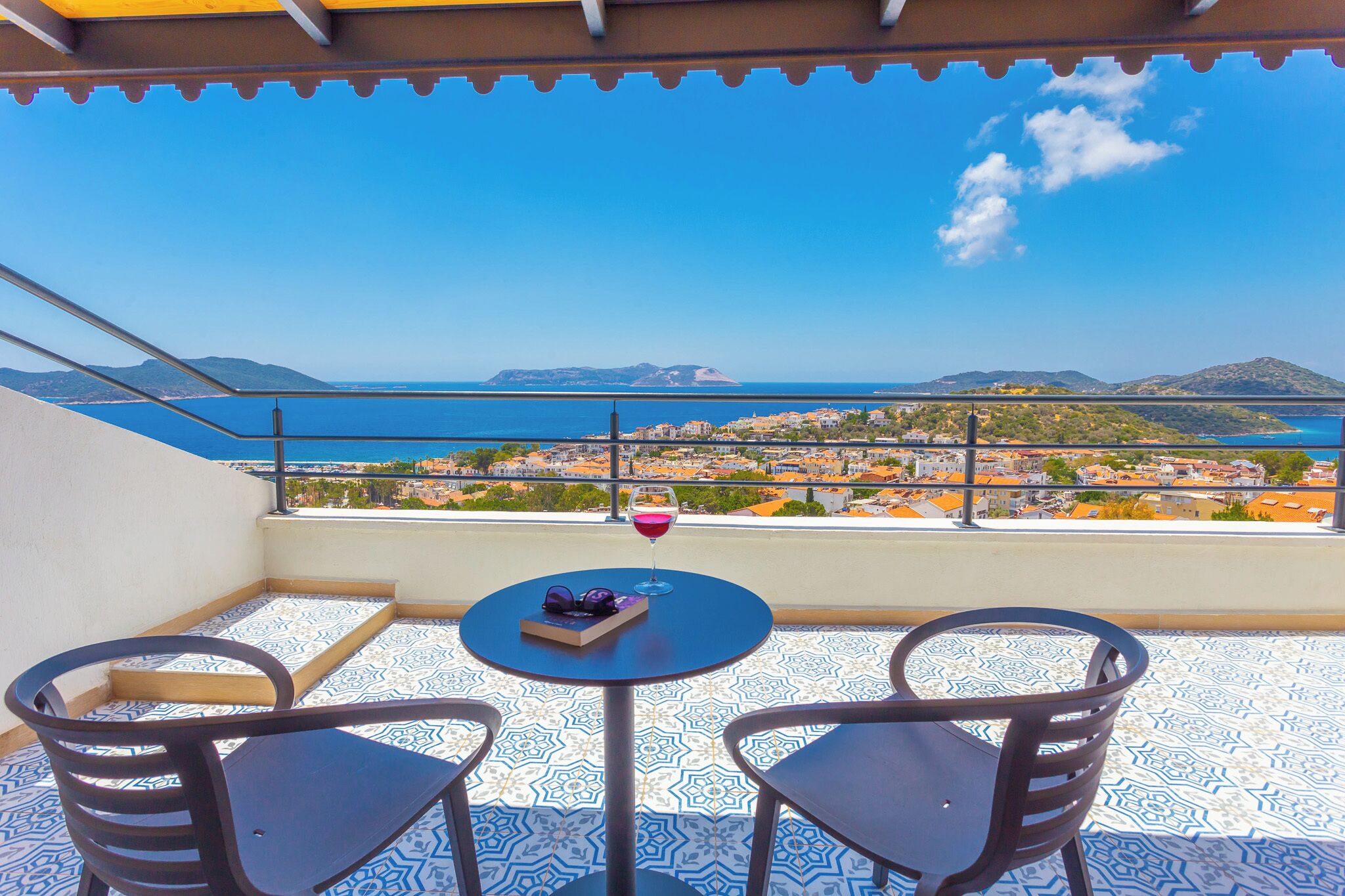 Ein Balkon mit zwei Stühlen und einem Tisch, mit Blick auf eine Küstenstadt und das Meer.