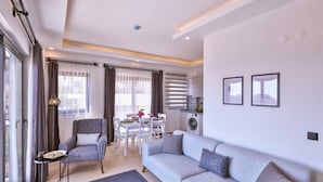 Un salon moderne avec un canapé gris, un coin repas comprenant une table et des chaises, une petite table d’appoint et un lave-linge à l’arrière-plan.