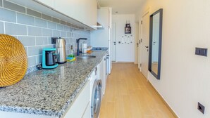 Une cuisine moderne dotée de plans de travail en granit, d’une machine à café, d’une bouilloire et d’un lave-linge.