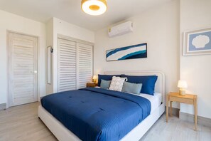 Une chambre à coucher comprenant un lit, des tables de chevet, un climatiseur et une œuvre d’art accrochée au mur.