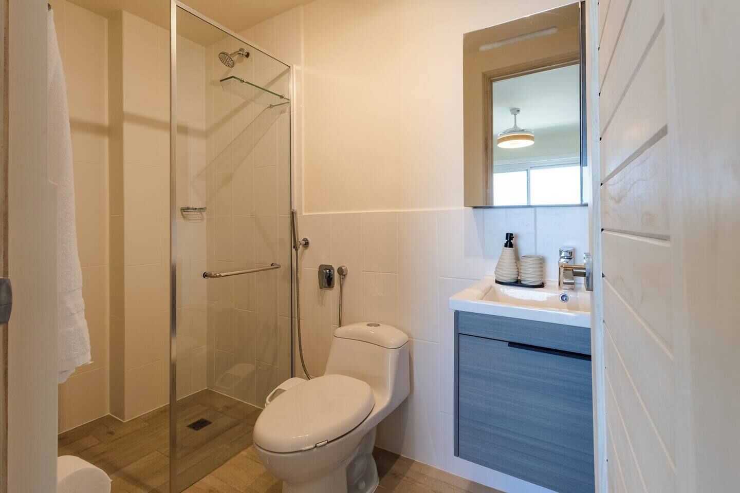 A bathroom with a glass shower enclosure, a toilet, and a sink with a mirror above.