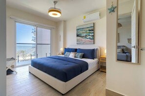 Ein Schlafzimmer mit Bett, Nachttisch, Wand-Klimaanlage, großem Fenster und Balkon.