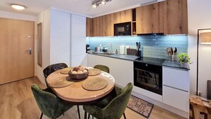 Una cocina moderna con armarios de madera, un microondas negro y una mesa de comedor redonda con sillas verdes.