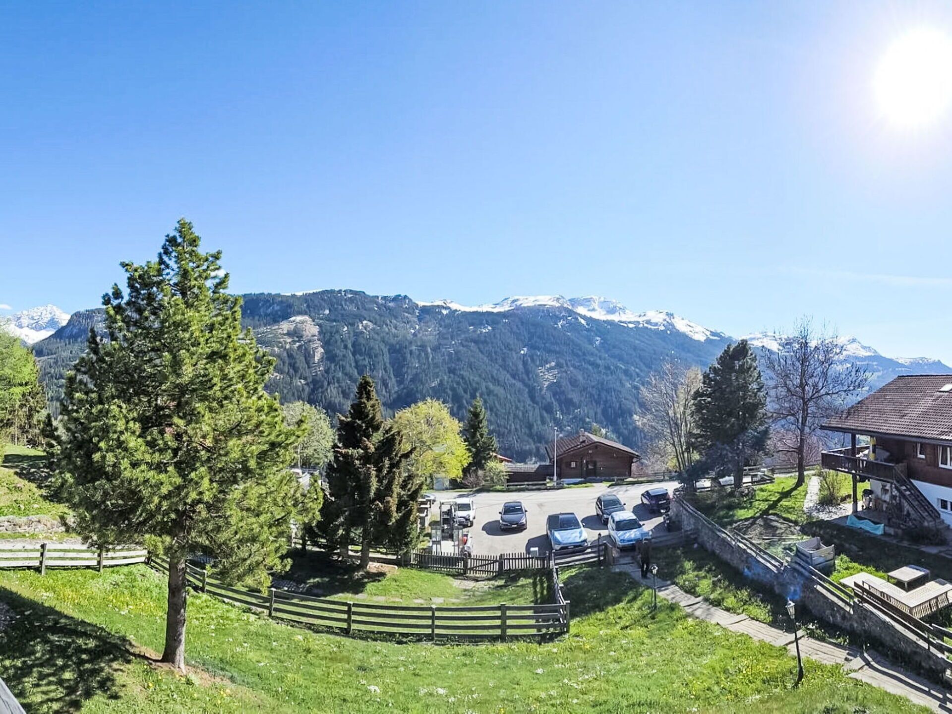 A mountain view with a parking area, a wooden building, and a fenced pathway.