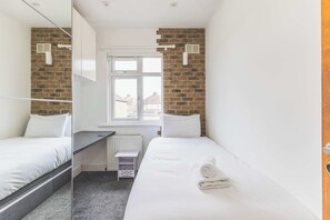 Ein kleines, modernes Hotelzimmer mit zwei Einzelbetten, einem Fenster, einer Heizung und einem kleinen Tisch.