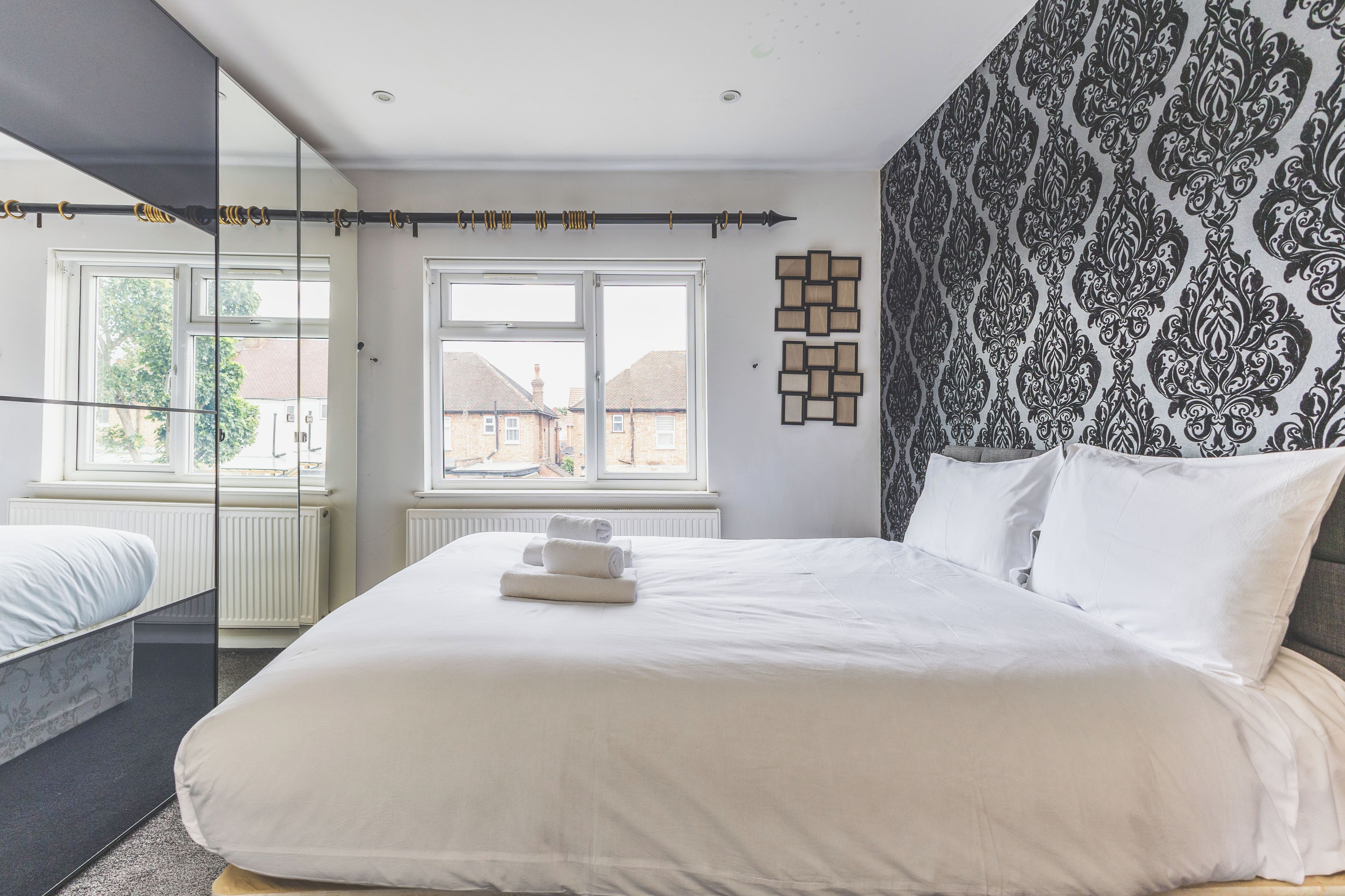 A hotel room with a large bed, a window with a view of buildings, a mirror, and a patterned wall.