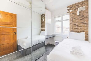 Ein Schlafzimmer mit Holztür, einem Spiegelkleiderschrank, einem Bett mit weißer Daunendecke und einer Ziegelwand.