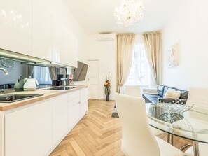 Eine moderne Küche mit Einbauofen, Kaffeemaschine und Fernseher. Es gibt einen Essbereich mit einem Glastisch und Stühlen.