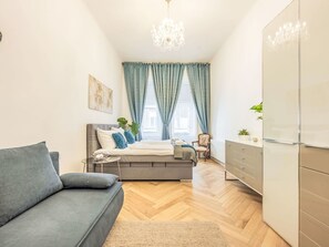 Ein modernes Schlafzimmer mit grauem Sofa, einem Bett mit blauen Vorhängen, einer Chandelierleuchtre und einem weißen Kleiderschrank.