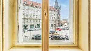 Una ventana con vistas a una calle que incluye una torre de iglesia, coches aparcados y edificios.