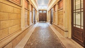 Un pasillo con piso de ladrillo, puertas de madera y techo con molduras decorativas.