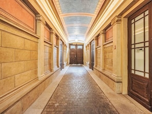 Ein Korridor mit Terrazzoboden, Holztüren und einer Decke mit dekorativen Stuckleisten.