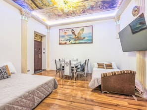 Ein Hotelzimmer mit zwei Betten, einem Schreibtisch, Stühlen, einem Fernseher und einem Wandgemälde an der Decke.