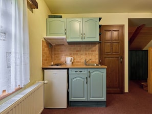 Eine kleine Küche mit Kühlschrank, Spüle und Herd. Ein Fenster mit Vorhängen und eine Tür zu einem anderen Raum.