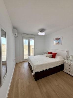 Ein Schlafzimmer mit Bett, Nachttisch und Blick durch eine Schiebetür in einen Außenbereich.