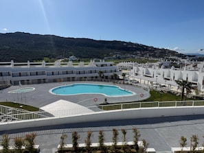 Ein modernes Hotel mit einem zentral gelegenen Schwimmbad, umgeben von weißen Gebäuden und einer hügeligen Landschaft im Hintergrund.