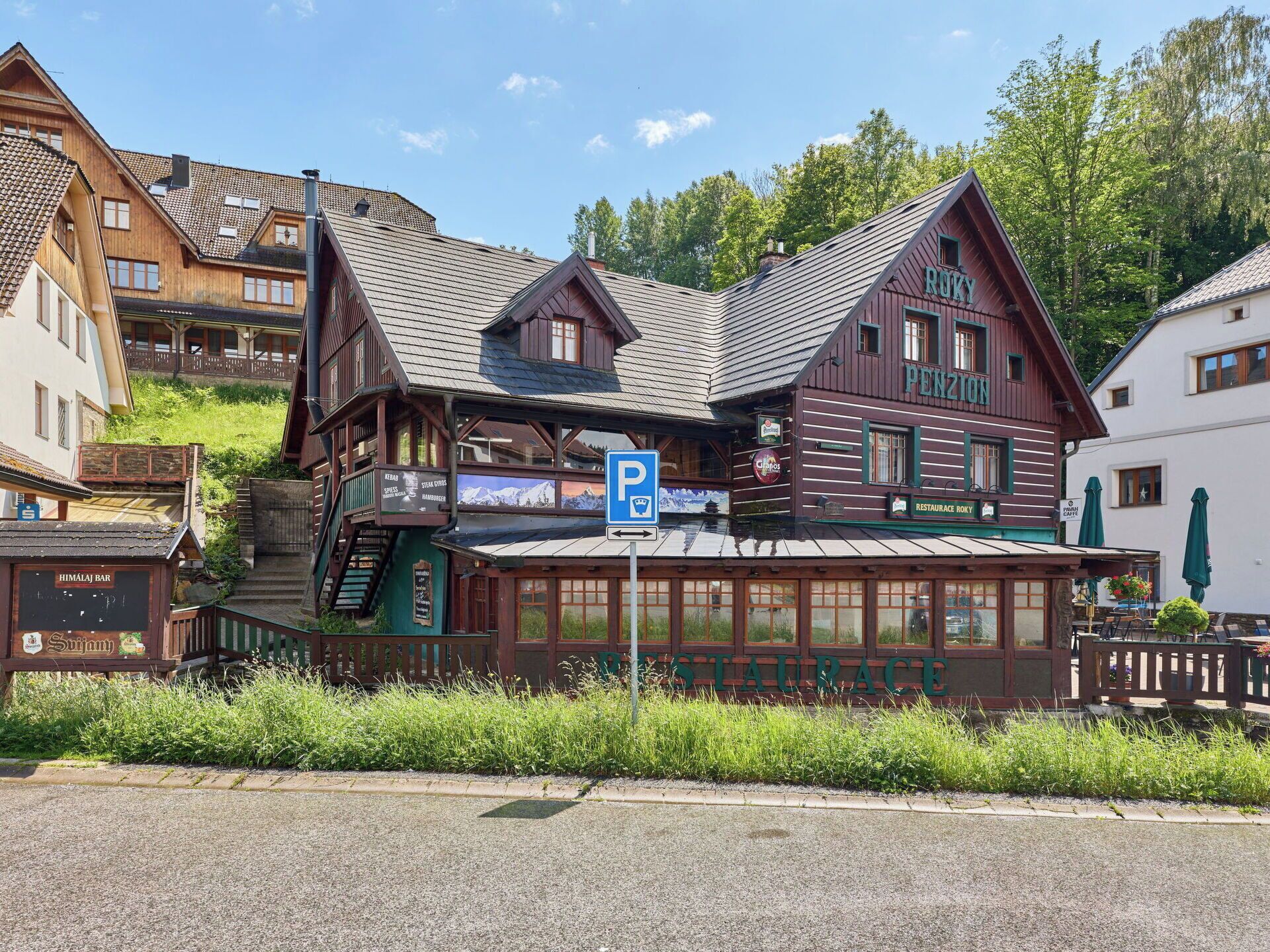 Un bâtiment traditionnel en bois, avec une enseigne indiquant la présence d’un restaurant, un escalier visible et un panneau indiquant un parking.