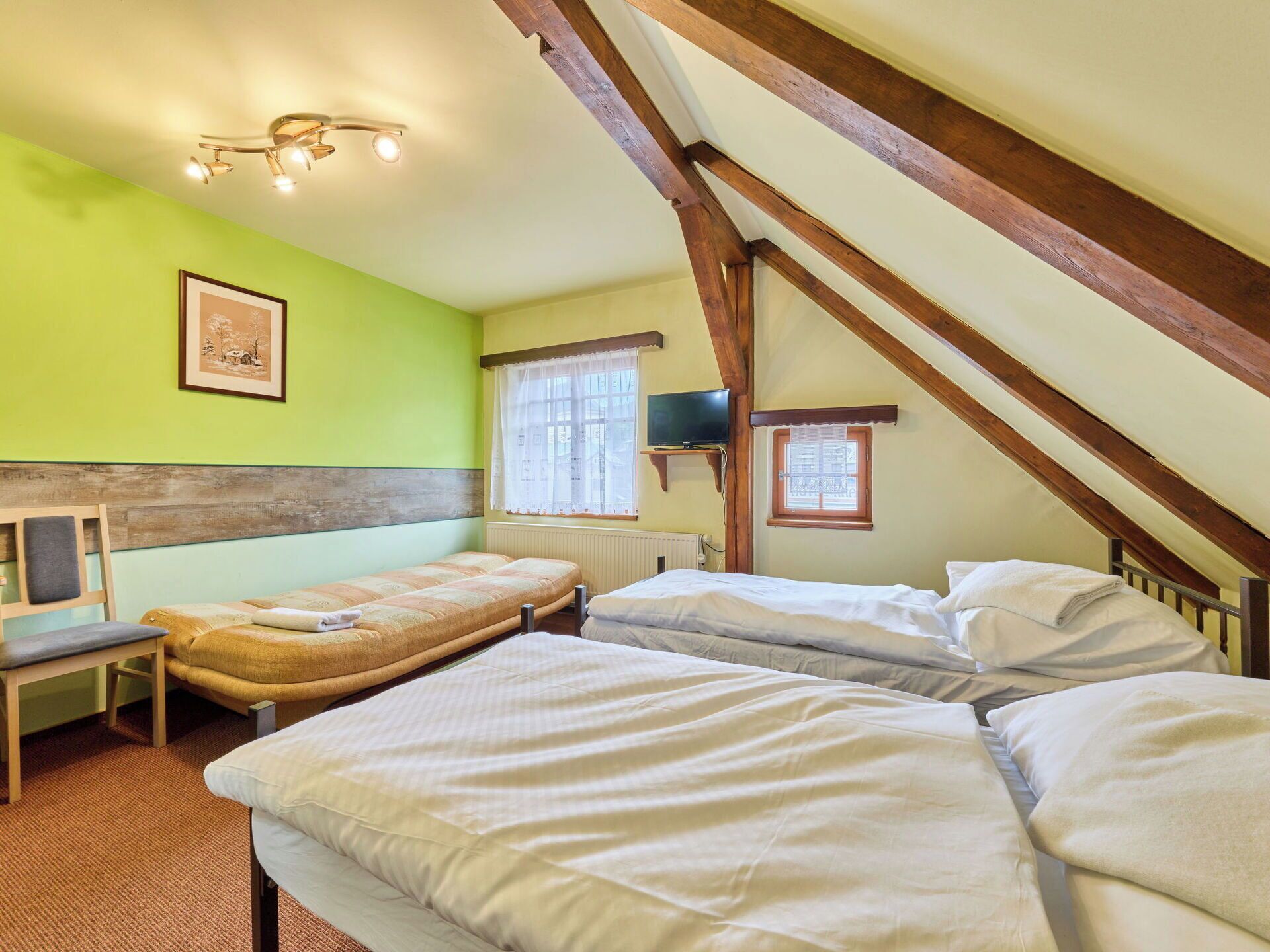 A room with two beds, a bench, a television, and a framed picture on the wall.