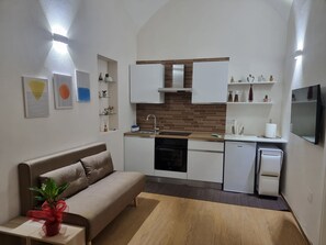 A compact living space with a kitchenette, a sofa, a small table with a plant, and wall-mounted artwork. - Quiet apartment in the city center, in a prime location, with an outdoor patio (Napoli)
