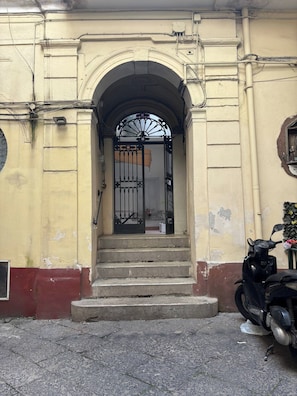 A building entrance with a gated archway, steps leading up to it, and a scooter parked outside. - Quiet apartment in the city center, in a prime location, with an outdoor patio (Napoli)