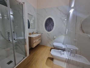 A bathroom with a glass shower enclosure, a wooden vanity, a round mirror, and a white toilet. - Quiet apartment in the city center, in a prime location, with an outdoor patio (Napoli)