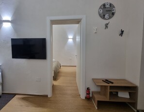 A room with a flat-screen TV, a wooden floor, a small wooden table, a clock, and a door leading to another room. - Quiet apartment in the city center, in a prime location, with an outdoor patio (Napoli)