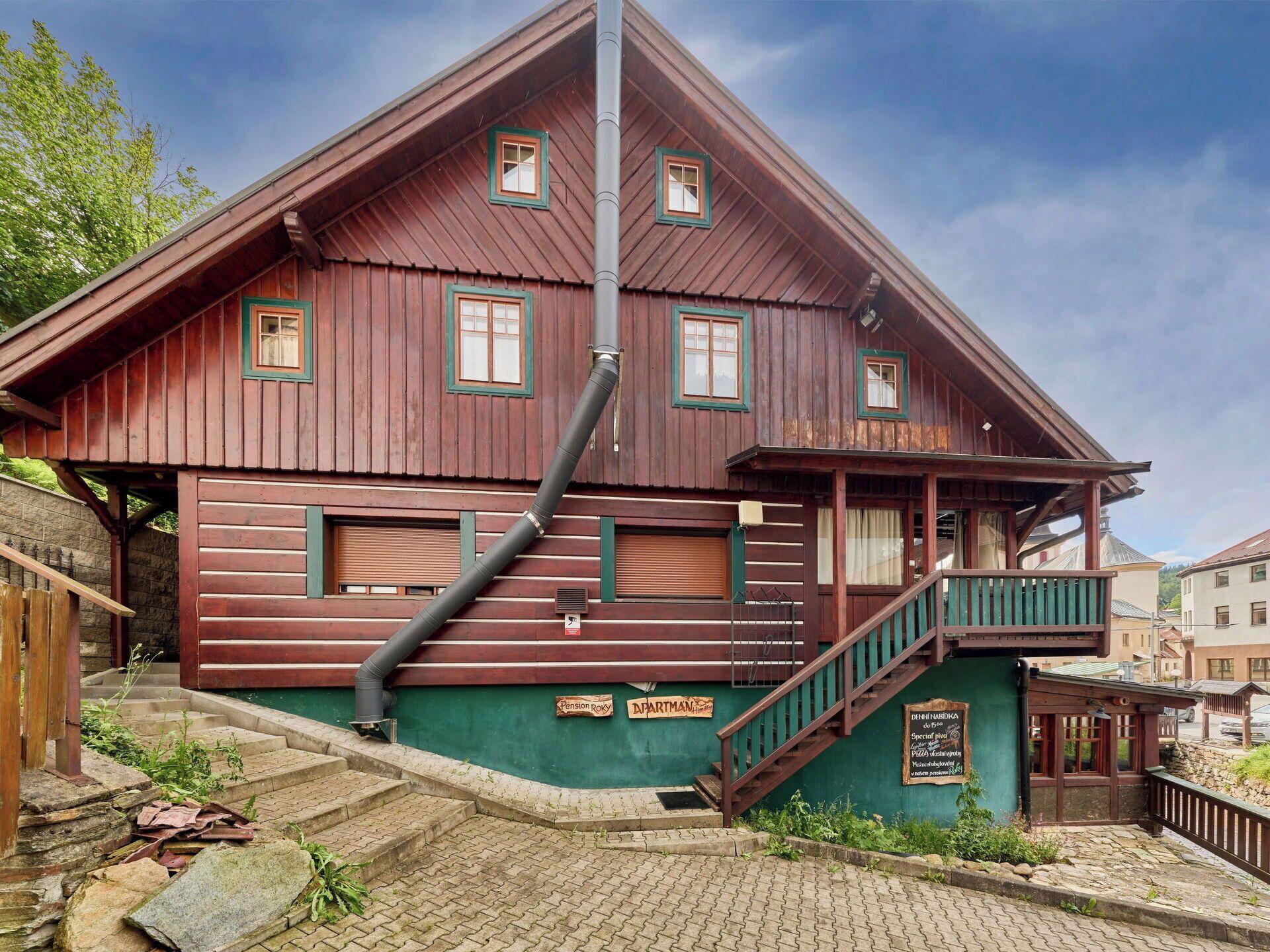 Ein traditionelles Holzhaus mit Balkon, Treppe und einem Schild, das ein Pension angibt.