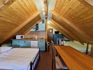 A compact attic bedroom with a bed, a wooden table, and a kitchenette. - Lovely apartment for 4 guests with WIFI and TV (Jilemnice)