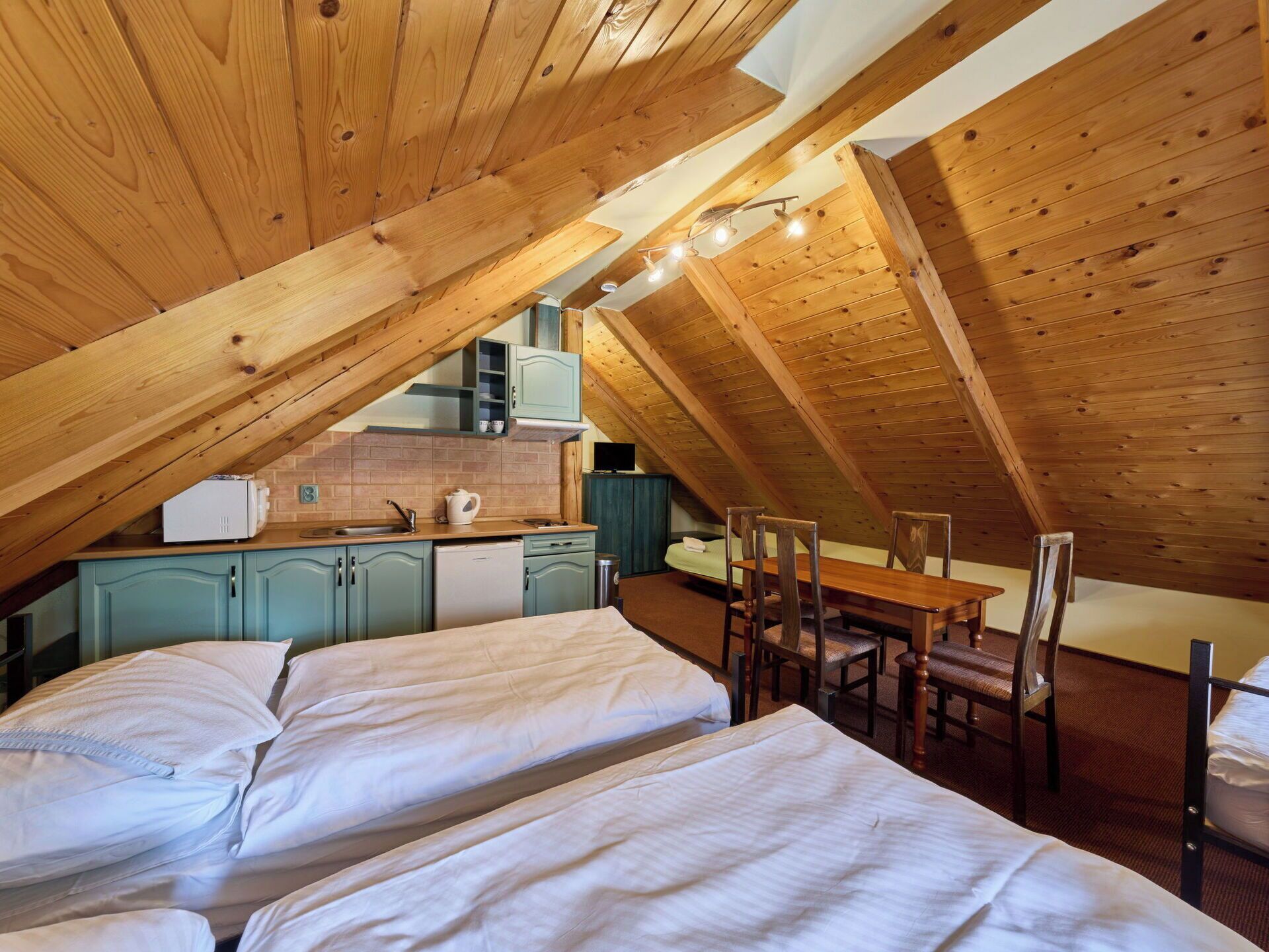 Un dormitorio acogedor en el ático con dos camas, una mesa de comedor y una kitchenette.