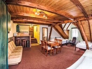 Ein gemütliches Schlafzimmer im Dachgeschoss mit Holzbalkendecke, einer Essecke mit Tisch und Stühlen, einem Sofa und einem Bett.