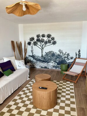 Ein Wohnzimmer mit einer Couch, zwei Holznachttischen, einem karierten Teppich, einem Gemälde einer Wüstenlandschaft und einem Holzhängelventilator.