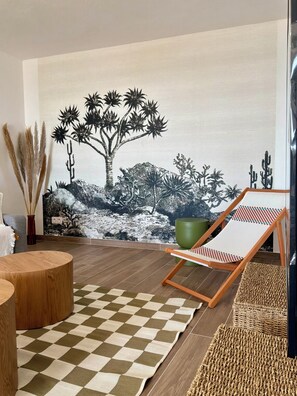 Ein Zimmer mit einem Schachbrettmuster-Teppich, einem Holztisch, einem grünen Blumentopf und einem Stuhl mit einem Schachbrettmuster-Kissen.