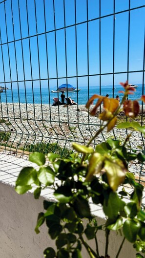 Blick auf einen Strand durch einen Metallzaun, mit einer Person, die sonnenbadet, und einer anderen, die spazieren geht.