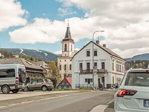 Un carrer amb cotxes aparcats, un edifici amb un balcó i una església amb una torre.