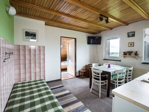 Een gezellige kamer met een geruit bed, een eettafel met stoelen, een aan de muur bevestigde televisie en een raam met uitzicht.