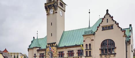 Un edificio histórico con una torre de reloj, ventanas en arco y techo verde.