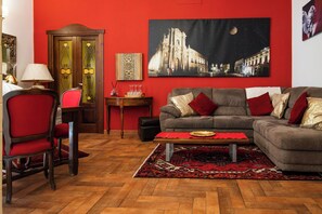 Ein Wohnzimmer mit roter Wand, einem großen Gemälde, einer Couch, einem Couchtisch und einem gemusterten Teppich.