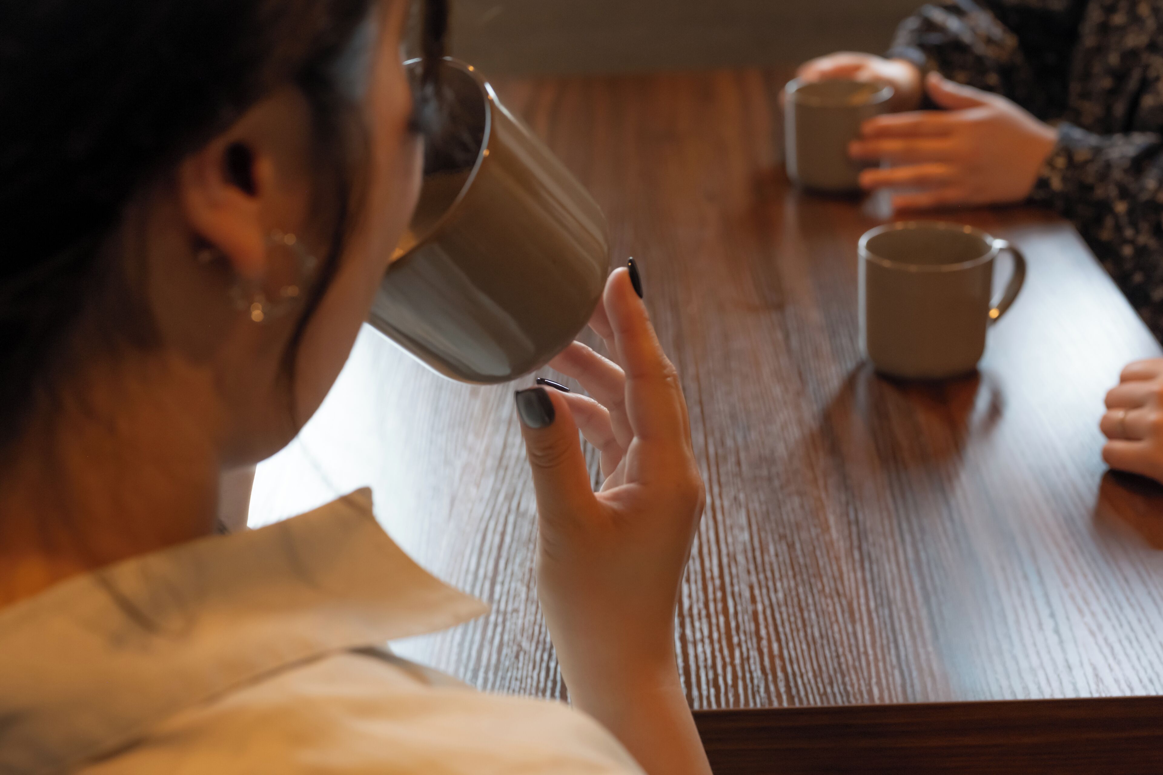 A person holding a mug, seated at a wooden table.