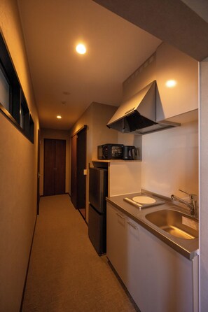 A narrow hallway leading to a compact kitchen with a refrigerator, microwave, and sink. - hoshinohikarinoyado Biei (Biei)